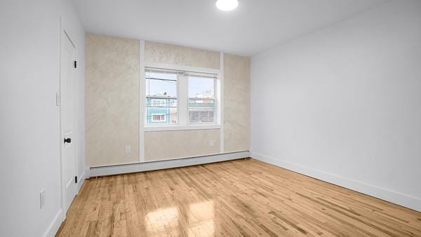 spare room featuring a baseboard radiator, baseboards, and wood finished floors