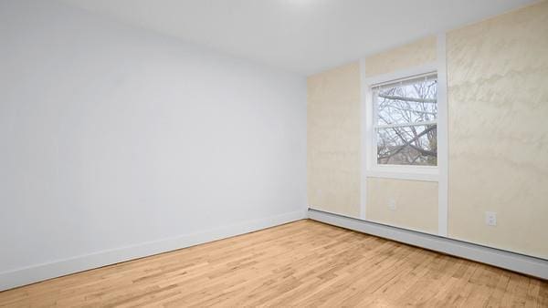 spare room with baseboards, a baseboard heating unit, and wood finished floors