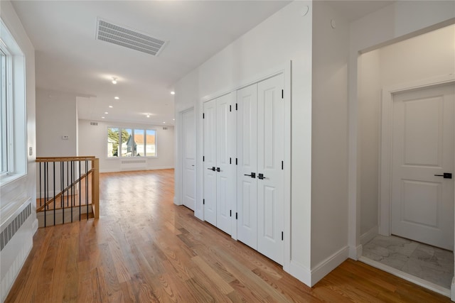 hallway featuring visible vents, an upstairs landing, light wood-style flooring, and radiator heating unit