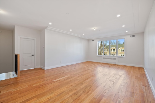 empty room featuring light wood-type flooring, visible vents, baseboards, and radiator heating unit