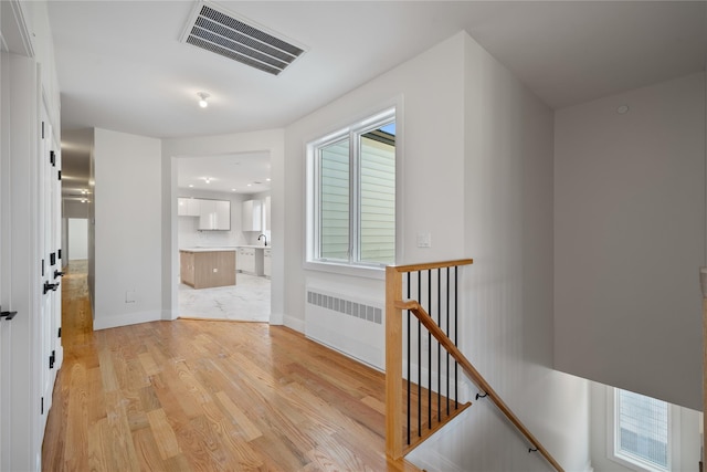 hallway with visible vents, baseboards, light wood-style flooring, radiator heating unit, and an upstairs landing