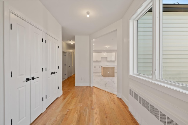 corridor with radiator heating unit, light wood-style floors, plenty of natural light, and baseboards