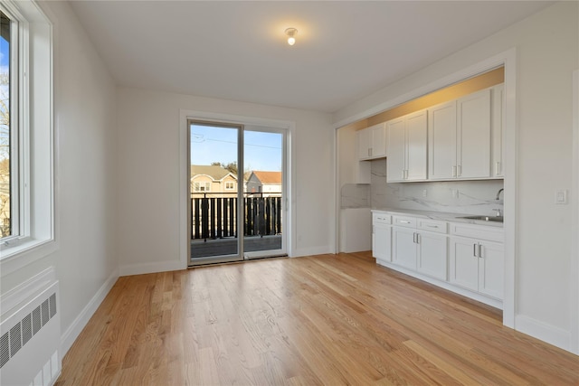 interior space featuring decorative backsplash, white cabinets, radiator, and light wood-style flooring