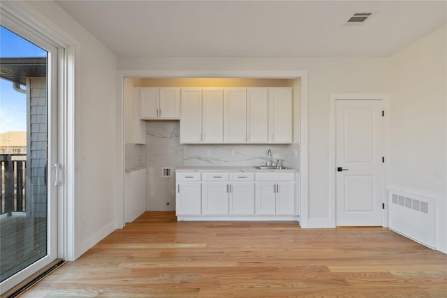 kitchen with a sink, visible vents, white cabinetry, and light wood finished floors