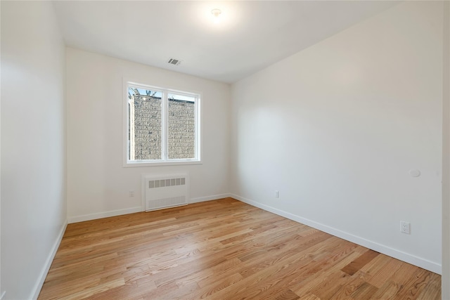 empty room with radiator heating unit, baseboards, visible vents, and light wood finished floors