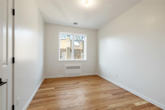 empty room with radiator, baseboards, visible vents, and light wood finished floors