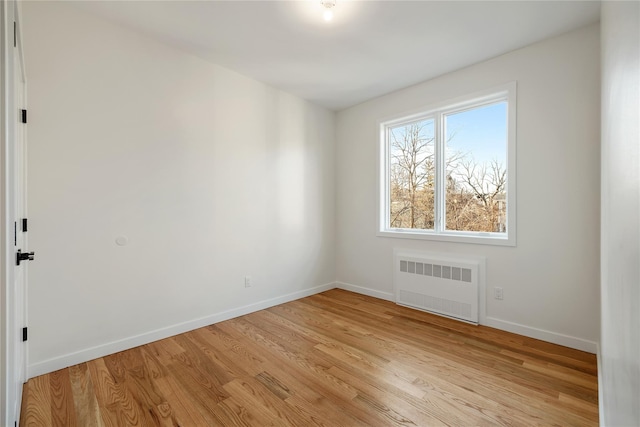 empty room featuring light wood-style flooring, radiator heating unit, and baseboards