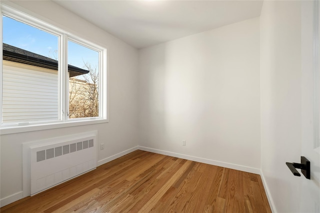 spare room featuring baseboards, radiator, and light wood finished floors