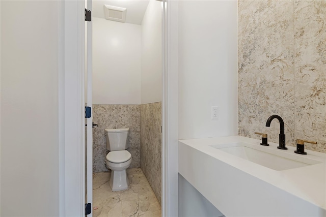 half bathroom featuring a wainscoted wall, toilet, tile walls, and a sink