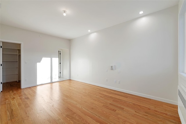 unfurnished bedroom with baseboards, light wood-style flooring, radiator heating unit, recessed lighting, and a spacious closet