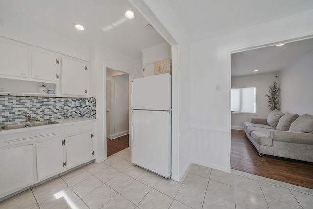 kitchen featuring light tile patterned flooring, a sink, white cabinetry, backsplash, and freestanding refrigerator