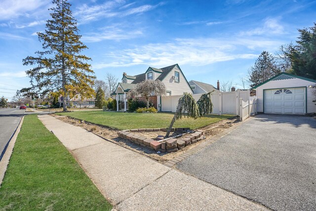 view of front of house featuring aphalt driveway, an outbuilding, a front yard, fence, and a garage