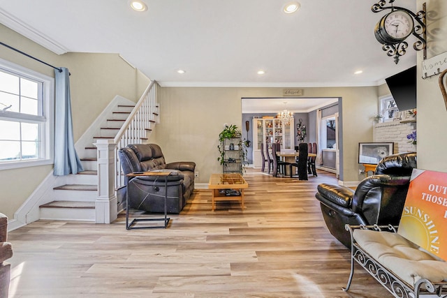 living area with a notable chandelier, crown molding, light wood-type flooring, and stairs