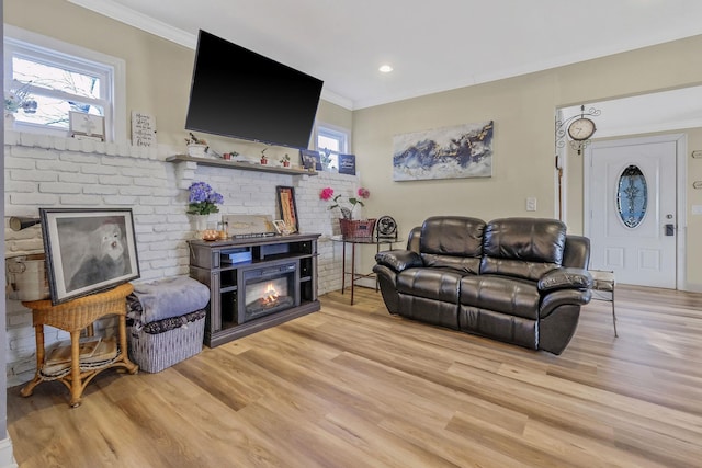 living room with wood finished floors, a healthy amount of sunlight, a glass covered fireplace, and ornamental molding