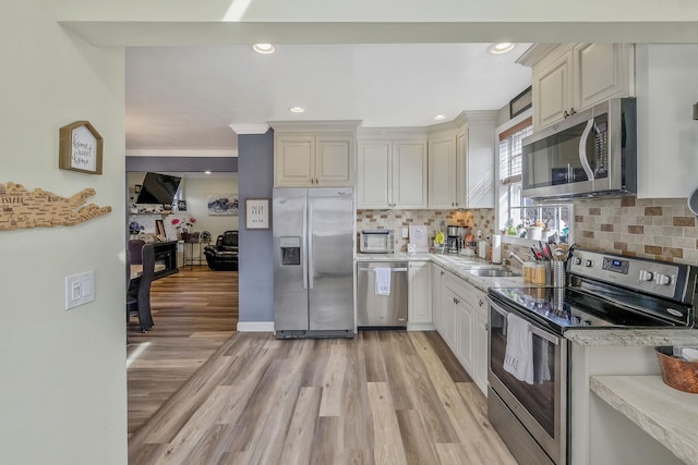 kitchen with a sink, light wood-style floors, backsplash, and stainless steel appliances