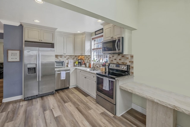 kitchen with backsplash, appliances with stainless steel finishes, light wood-type flooring, and a sink