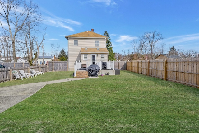 rear view of property with a deck, a yard, a fenced backyard, and a chimney