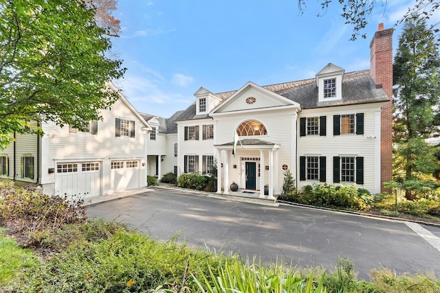 view of front of house with an attached garage, a chimney, and driveway