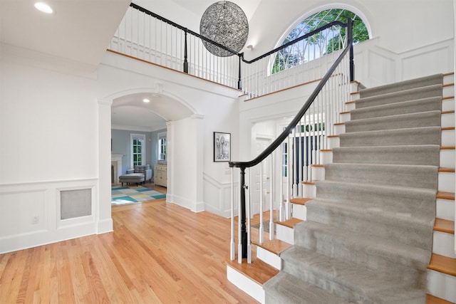 stairs featuring arched walkways, a decorative wall, ornamental molding, and wood finished floors