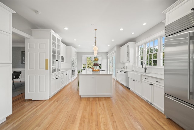 kitchen featuring a center island, appliances with stainless steel finishes, light wood-style floors, white cabinets, and a sink