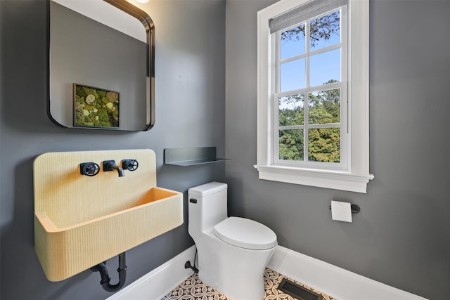 half bath featuring toilet, baseboards, and a sink