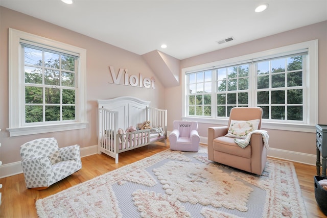 bedroom featuring recessed lighting, baseboards, a nursery area, and wood finished floors