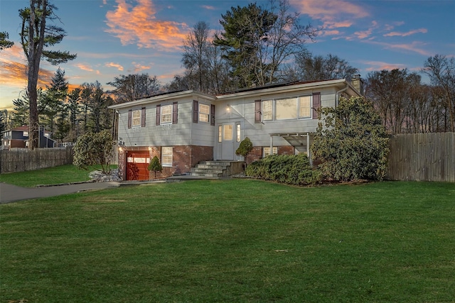 split foyer home featuring a front yard, an attached garage, fence, and brick siding