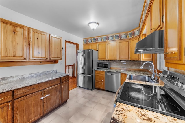 kitchen with backsplash, light stone countertops, under cabinet range hood, appliances with stainless steel finishes, and a sink