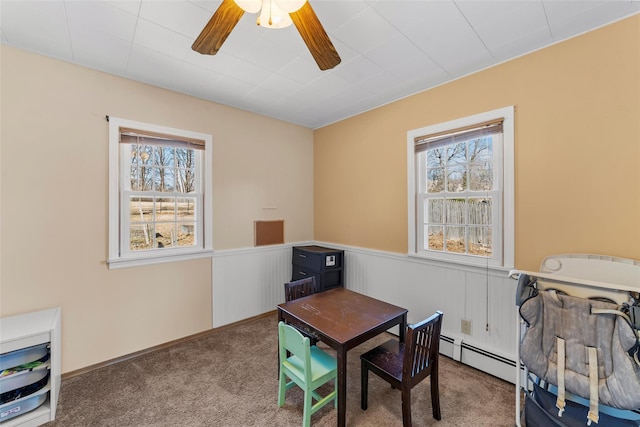 carpeted home office with a baseboard radiator, a healthy amount of sunlight, a wainscoted wall, and a ceiling fan