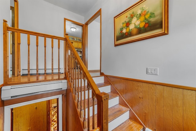 stairway with a wainscoted wall, baseboard heating, and wooden walls