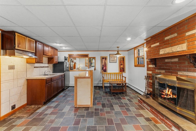 kitchen with a sink, a fireplace, light countertops, a paneled ceiling, and baseboards