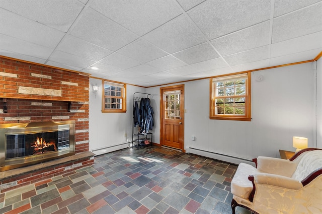 living room with baseboard heating, a brick fireplace, crown molding, and a drop ceiling