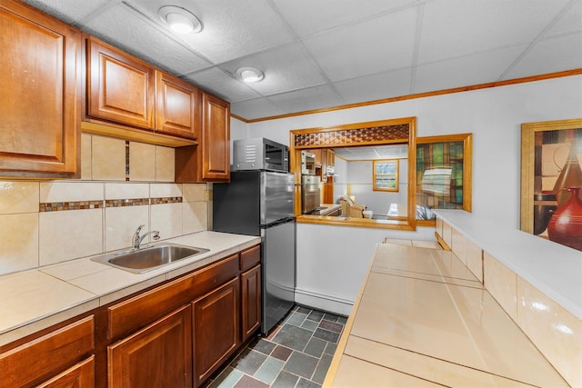 kitchen featuring a sink, a paneled ceiling, appliances with stainless steel finishes, tasteful backsplash, and baseboard heating