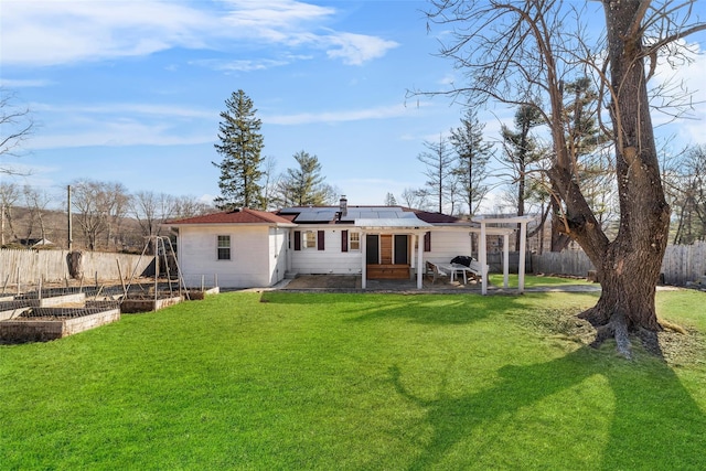 rear view of house featuring solar panels, a lawn, a fenced backyard, a garden, and a patio area