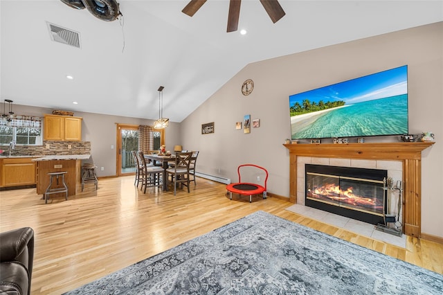 living room with visible vents, light wood-type flooring, lofted ceiling, a fireplace, and a baseboard radiator