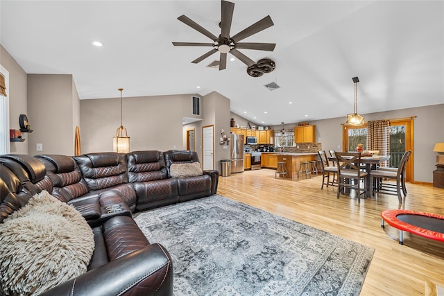 living area featuring light wood finished floors, visible vents, a ceiling fan, and vaulted ceiling