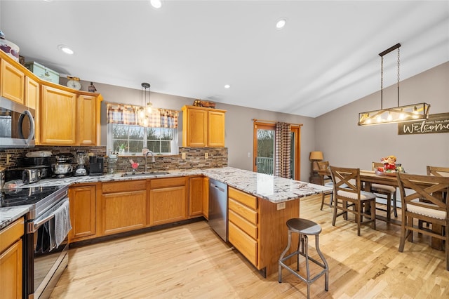 kitchen featuring appliances with stainless steel finishes, light wood-style floors, a peninsula, and a sink