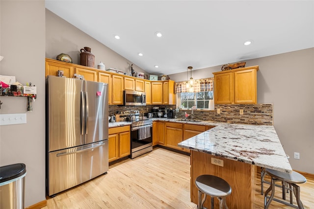 kitchen featuring a peninsula, lofted ceiling, a sink, stainless steel appliances, and light wood-style floors