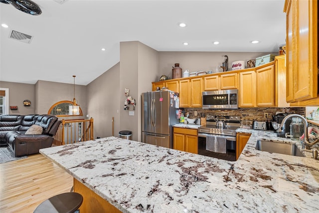 kitchen featuring visible vents, a sink, stainless steel appliances, light stone countertops, and vaulted ceiling