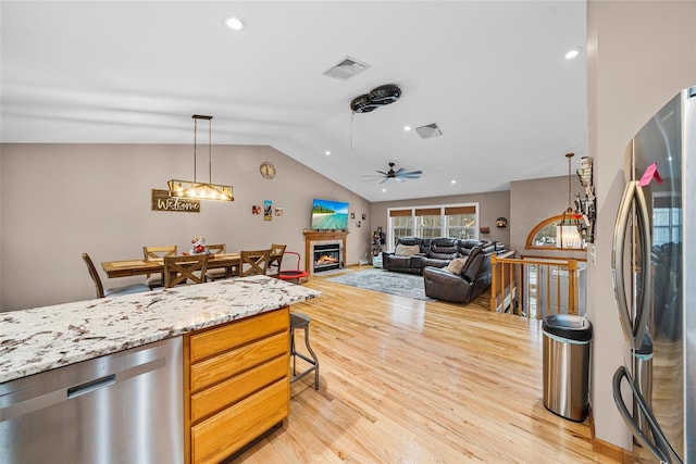 kitchen with light wood-type flooring, visible vents, a glass covered fireplace, stainless steel appliances, and vaulted ceiling