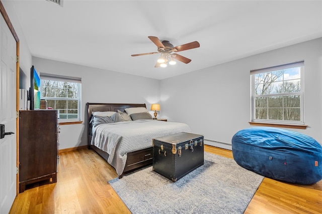 bedroom with ceiling fan, a baseboard heating unit, baseboards, and wood finished floors