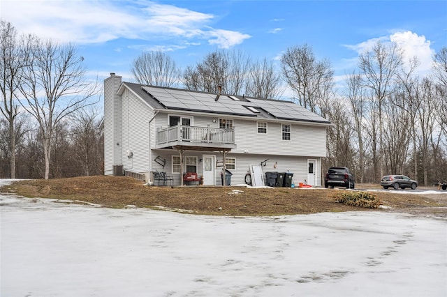 rear view of house featuring central air condition unit, solar panels, a deck, and a chimney