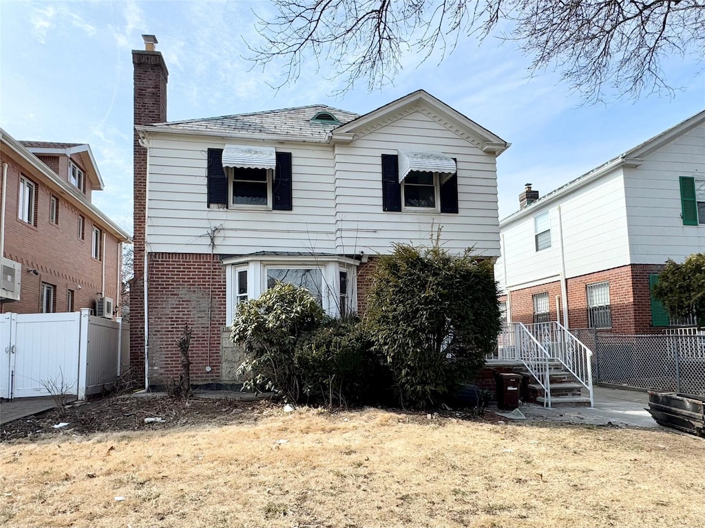 rear view of house featuring a chimney, fence, and brick siding