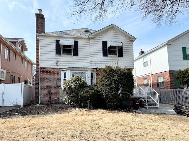 rear view of house featuring a chimney, fence, and brick siding