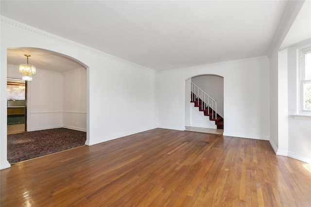 unfurnished room featuring hardwood / wood-style floors, crown molding, stairway, and arched walkways