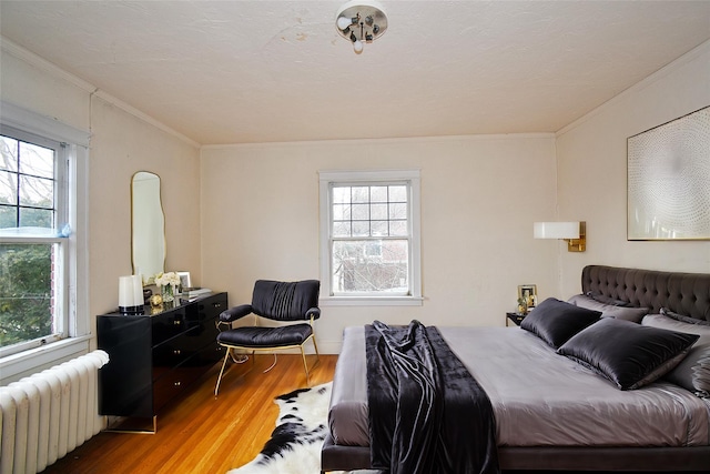 bedroom with multiple windows, radiator heating unit, wood finished floors, and crown molding