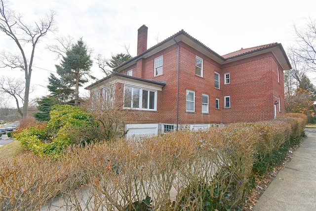 view of side of home with a tiled roof, brick siding, and a chimney