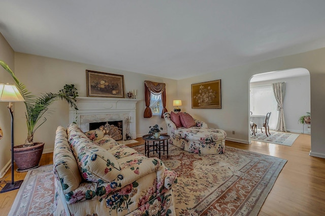 living area featuring a fireplace, baseboards, arched walkways, and wood finished floors