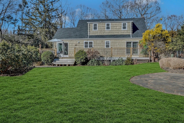 rear view of house with a patio, a deck, a lawn, and roof with shingles