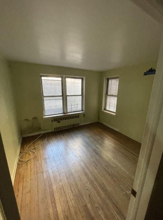 spare room with radiator heating unit, wood finished floors, and a healthy amount of sunlight